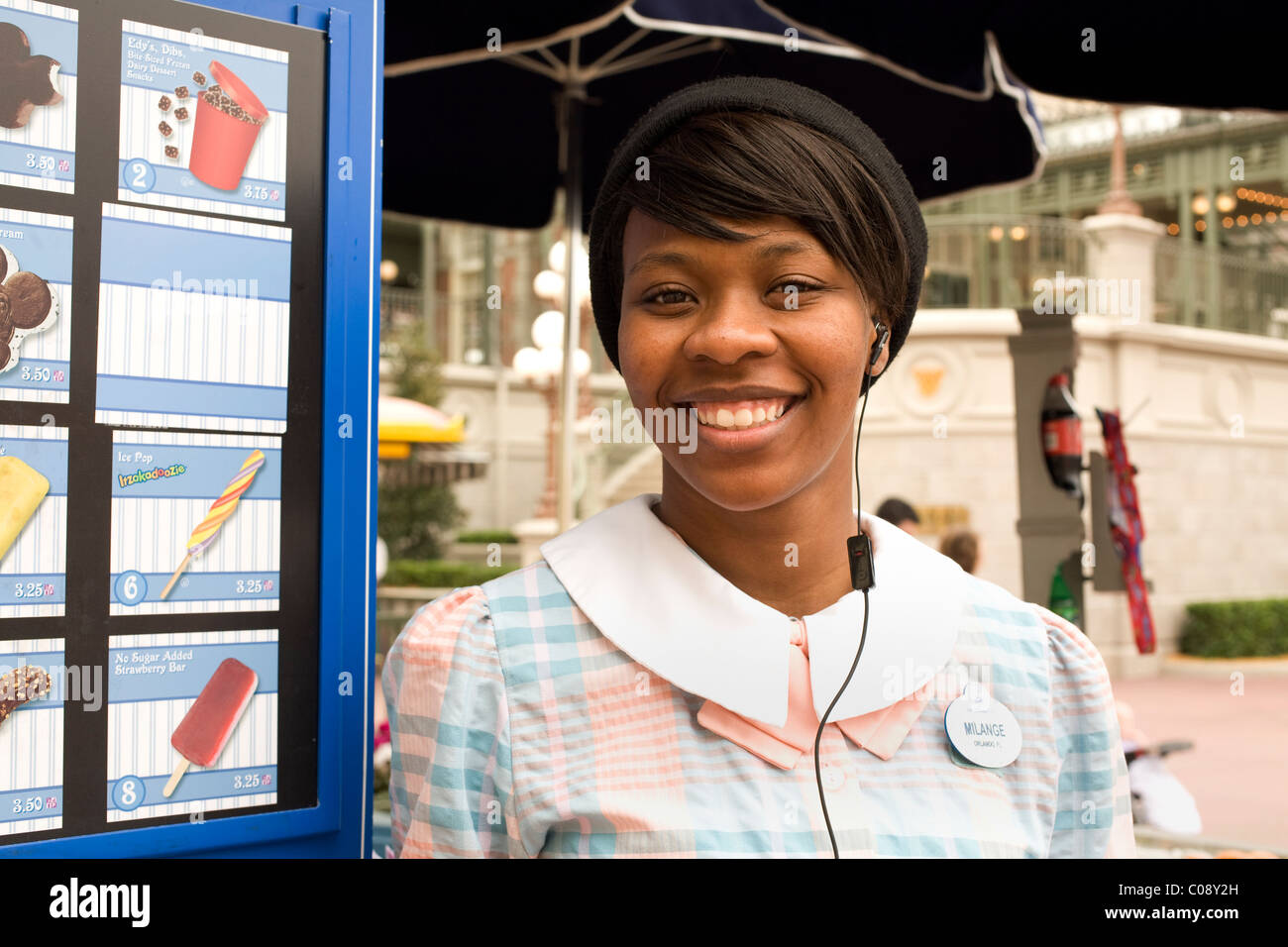Young African American Frau grüßt Eis-Kunden mit einem Lächeln im Disney World Magic Kingdom in Orlando, Florida. Stockfoto