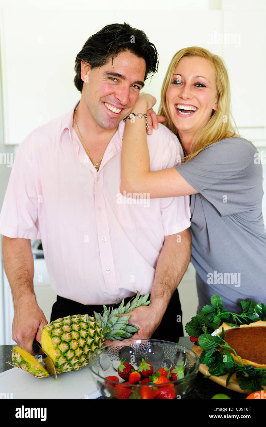 Man schneidet eine Ananas, junge Frau, die an seine Schulter gelehnt Stockfoto