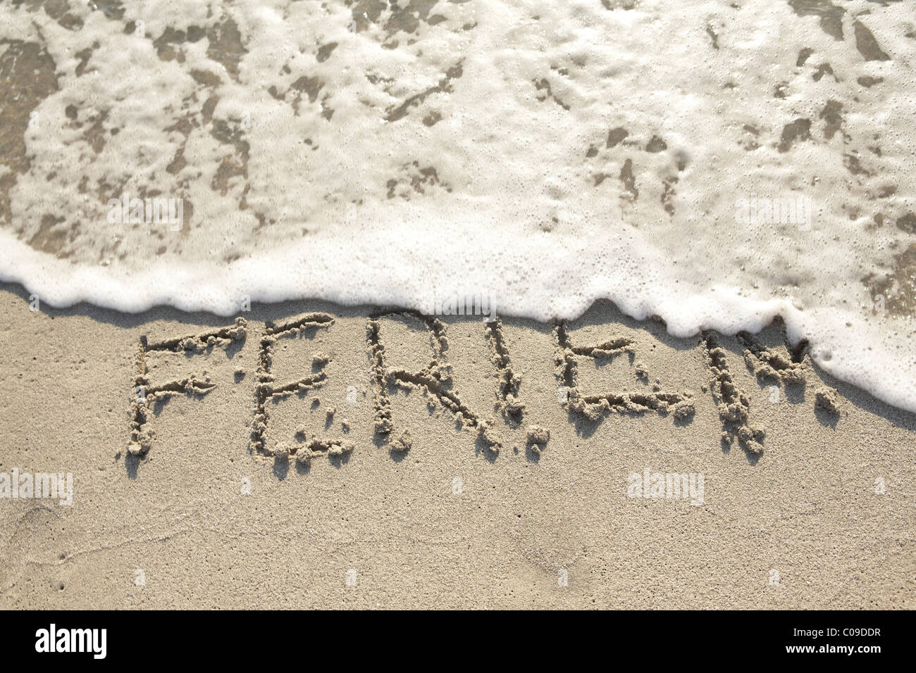 Ferien, Deutsch für Urlaub, geschrieben im nassen Sand von einer Welle weggespült Stockfoto