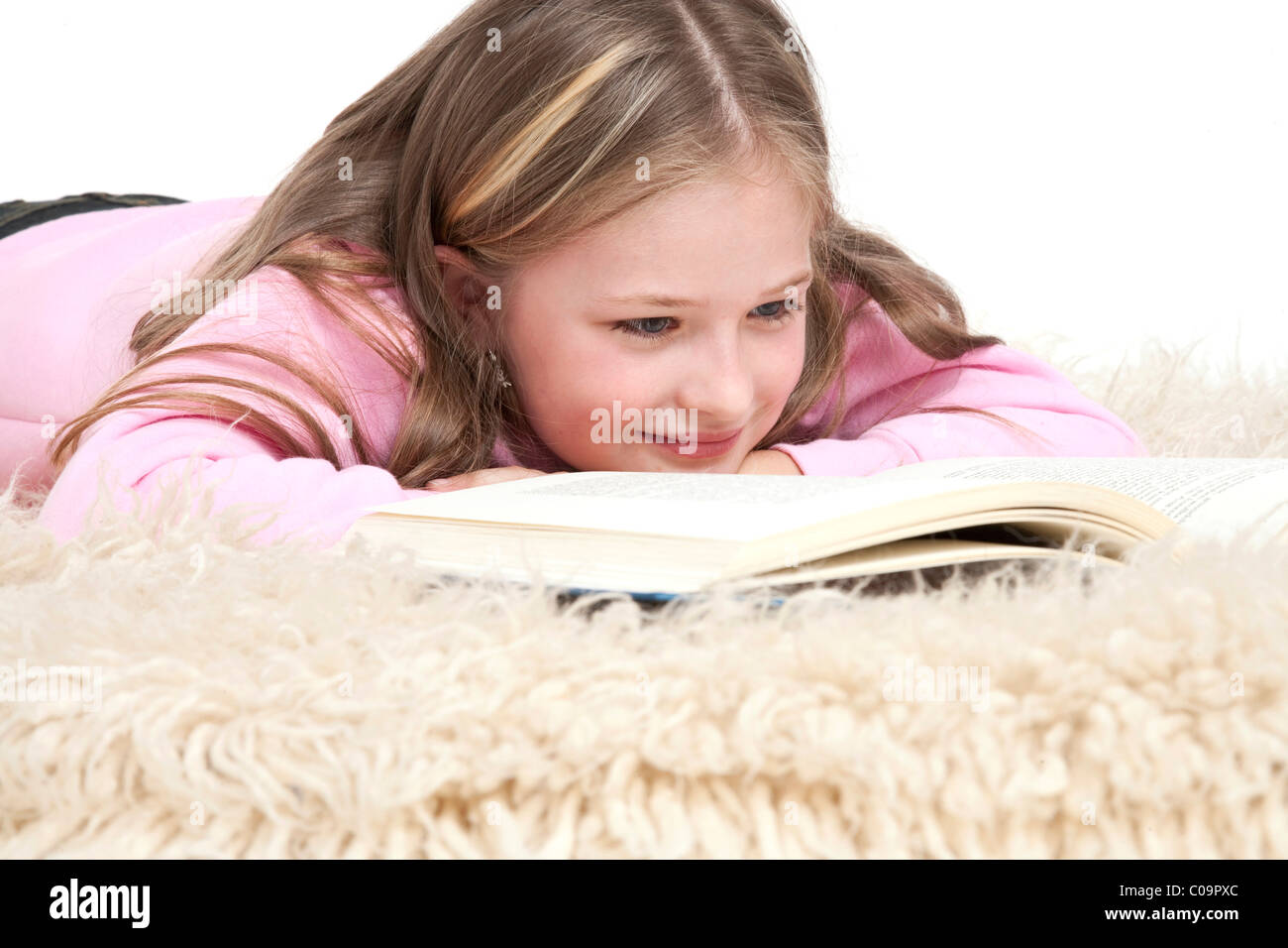 Mädchen, 8 Jahre, auf ein Shag Teppich liegen und ein Buch zu lesen Stockfoto