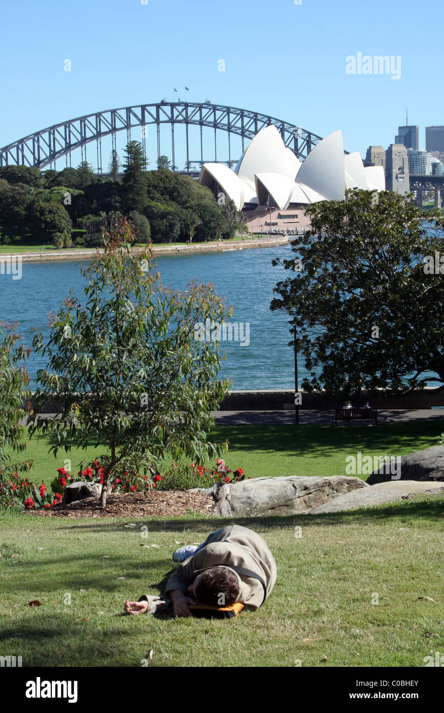 Eine Person nimmt einen Rest auf dem Rasen des Königlichen Botanischen Garten in Sydney mit Opernhaus und Harbour Bridge im Hintergrund. NSW, Australien. Stockfoto