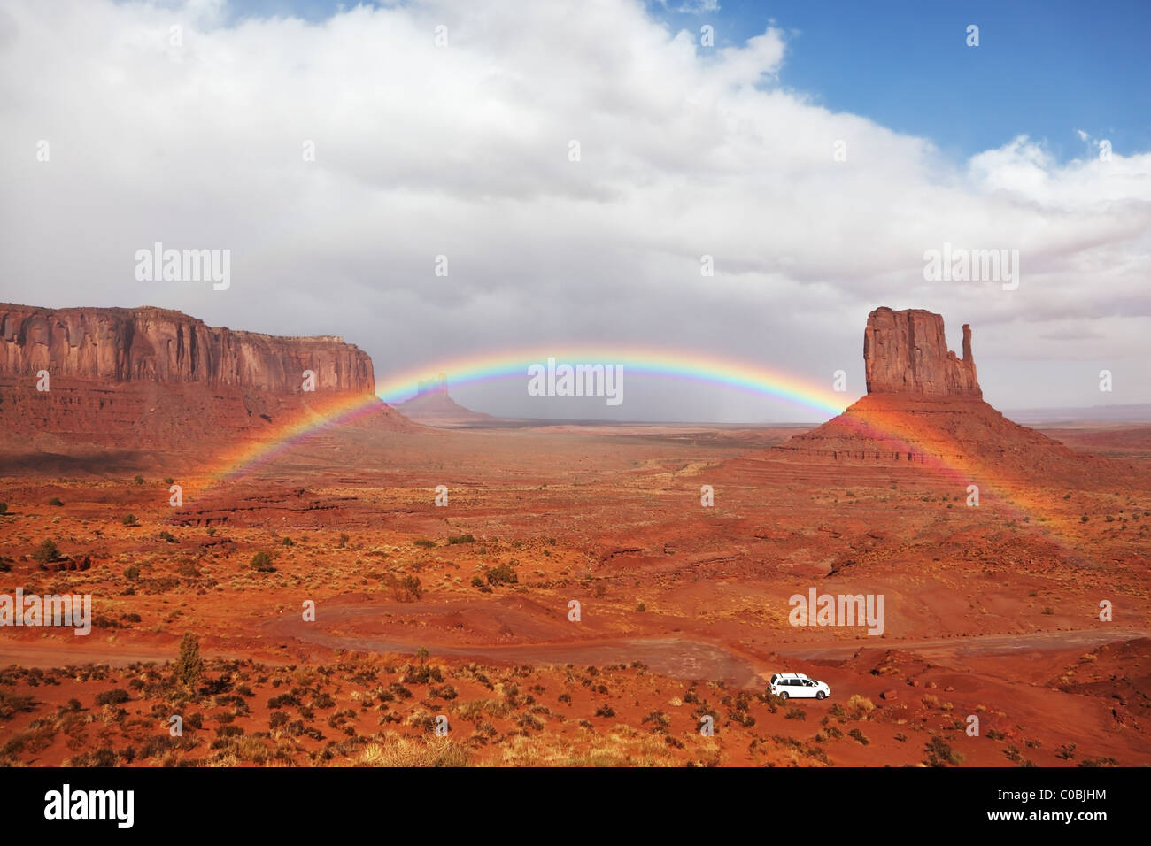 Ein weißes Auto unter einem Regenbogen in der roten Wüste. Die berühmte "Handschuhe" im Monument Valley nach dem Regen Stockfoto