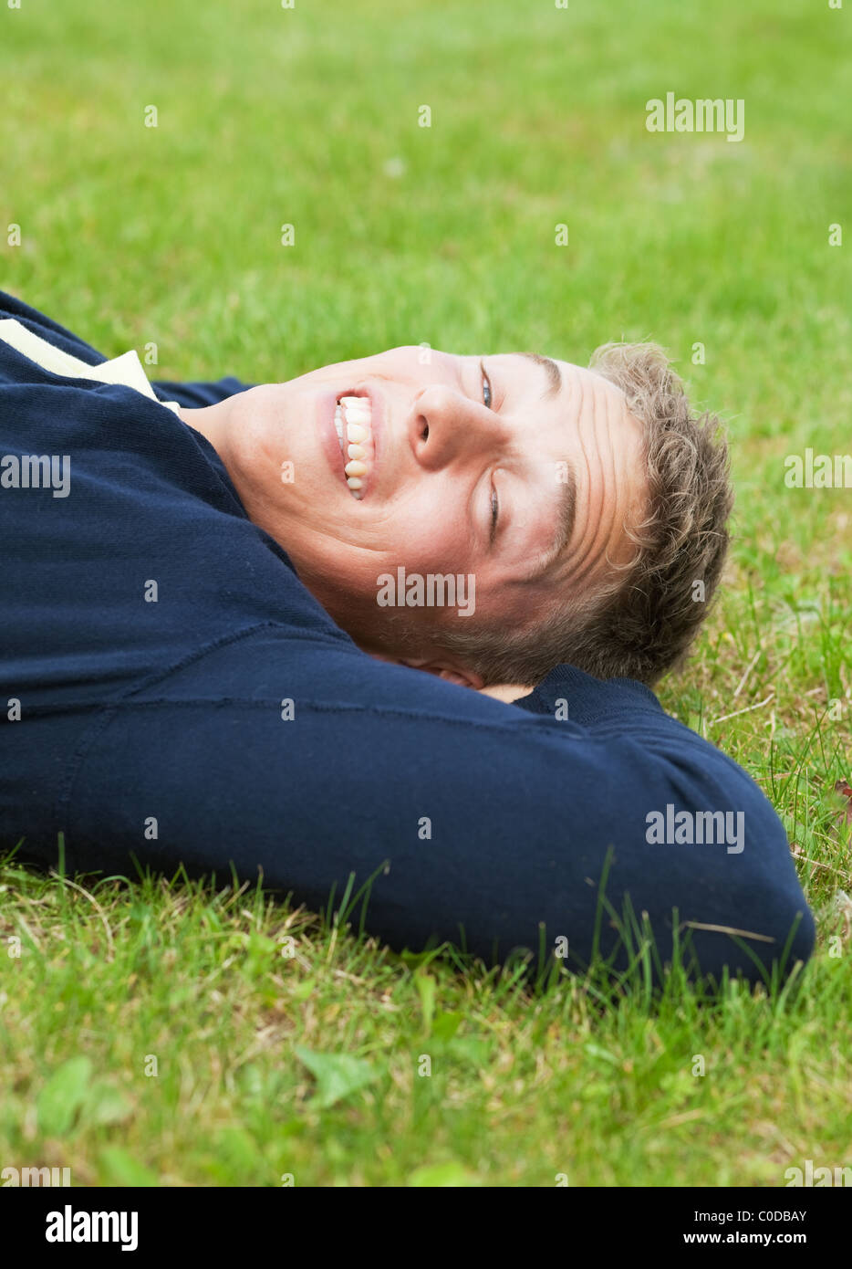 Junge blonde Kerl liegen auf dem Rasen, geschlitzten Augen wegen hellem Sonnenlicht Stockfoto