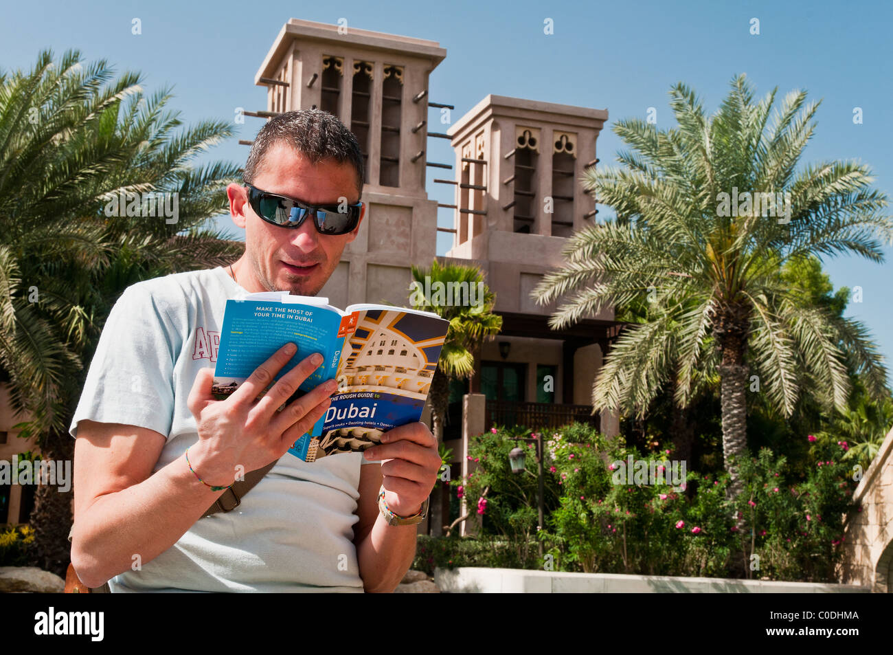 Tourist-Mann liest einen Reiseführer Dubai im Madinat Jumeirah mit Windtürme im Hintergrund, Dubai, Vereinigte Arabische Emirate Stockfoto