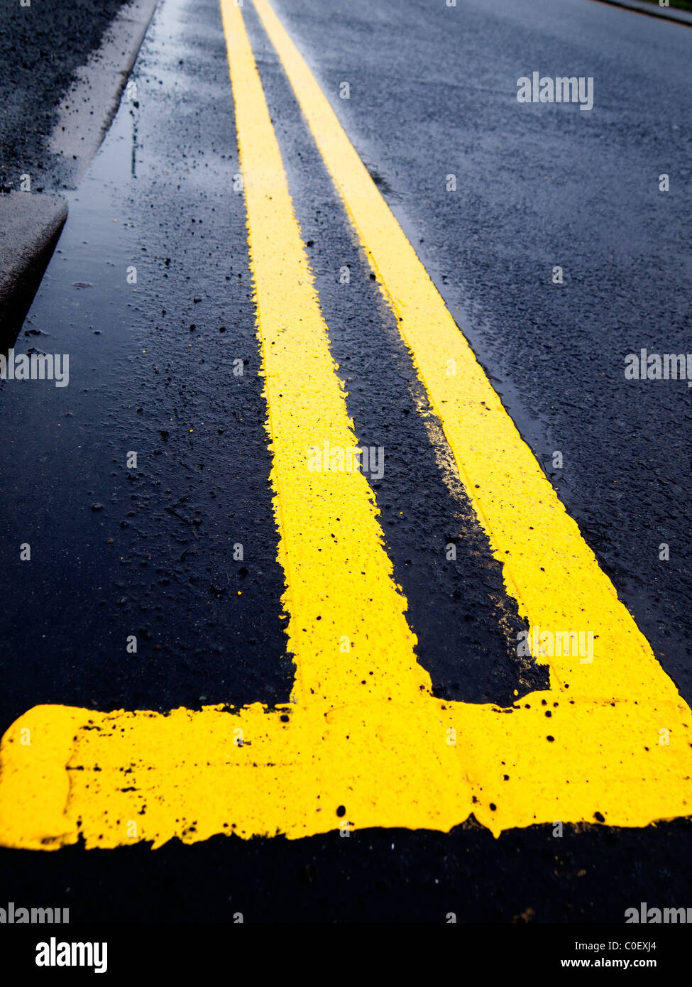 Straße, die Kennzeichnung einer frisch gestrichenen doppelten gelben Linie auf nasser Fahrbahn Stockfoto