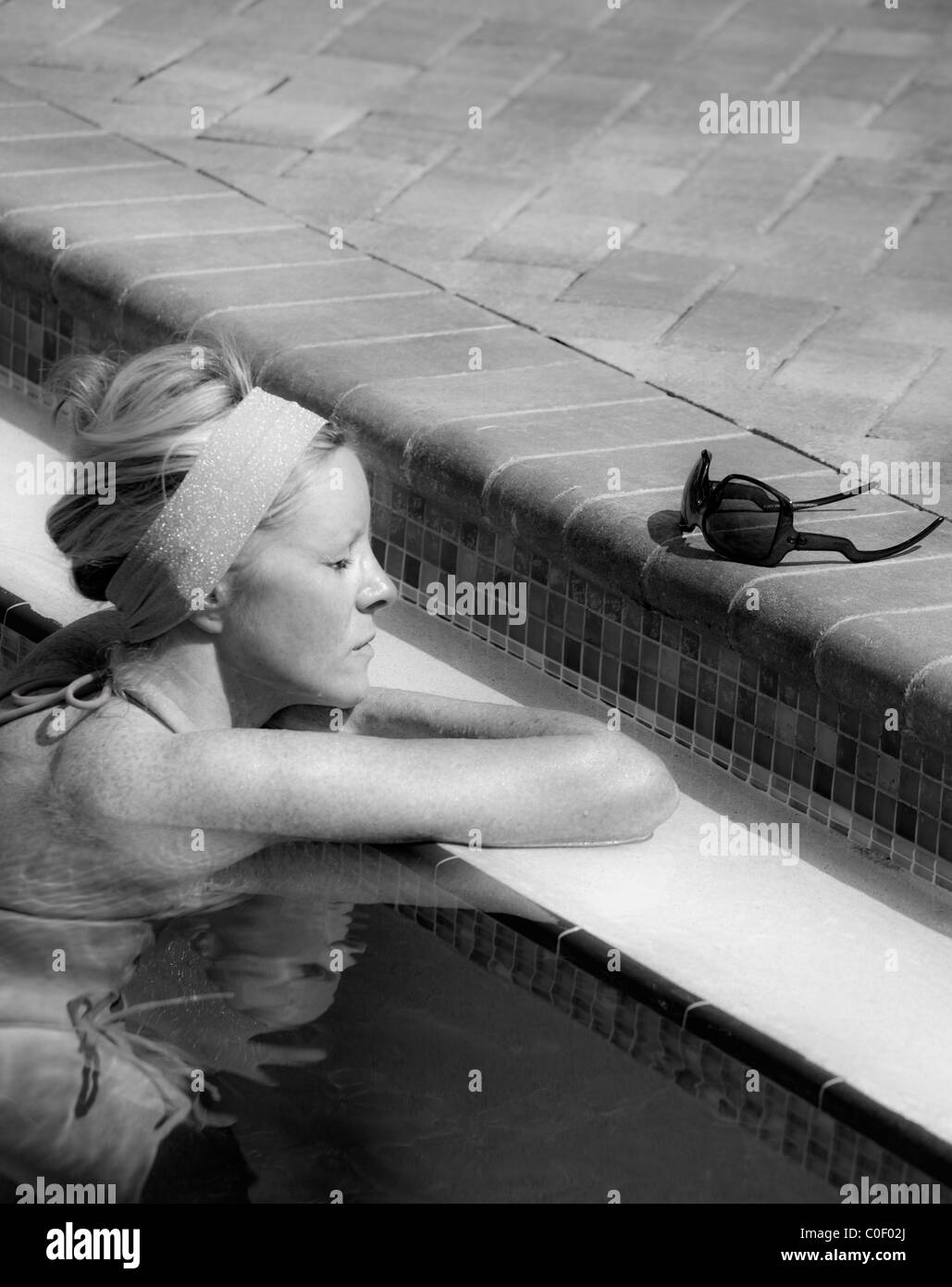 MONO-KONZEPT-BILD DER FRAU IN EINEN POOL MIT MAIN ENTSPANNEN/CHILLEN IM FOKUS SONNENBRILLEN Stockfoto