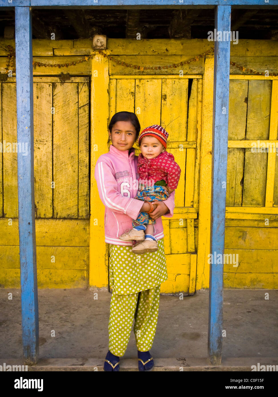 Nepalesische Mädchen hält ein kleines Kind vor einem Hauseingang in Nepal. Stockfoto