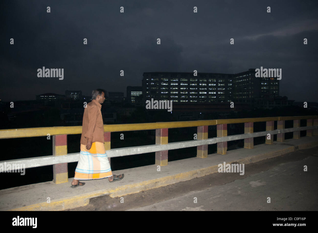 Ein Bangladeshi Mann geht über eine Brücke am Stadtrand von Dakar am frühen Abend mit einer Textilfabrik im Hintergrund Stockfoto