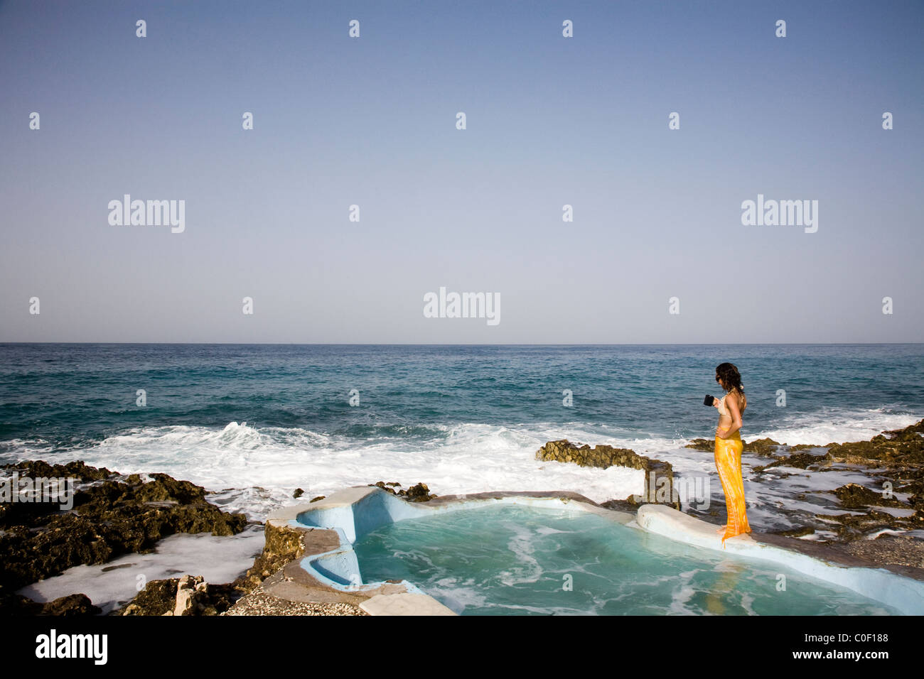 Eine Frau trinkt Kaffee am Rande einer Oceanside-Pool mit Blick auf das blaue Wasser. Stockfoto