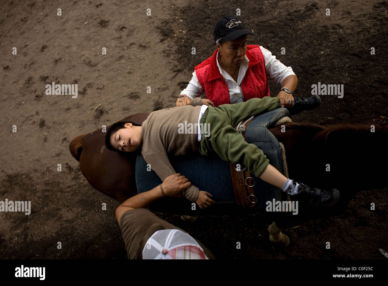 Equine Therapeuten führen ein Junge, der infantilen zerebralen Lähmung durch Übungen leidet, wie er auf dem Rücken eines Pferdes Durin liegt Stockfoto