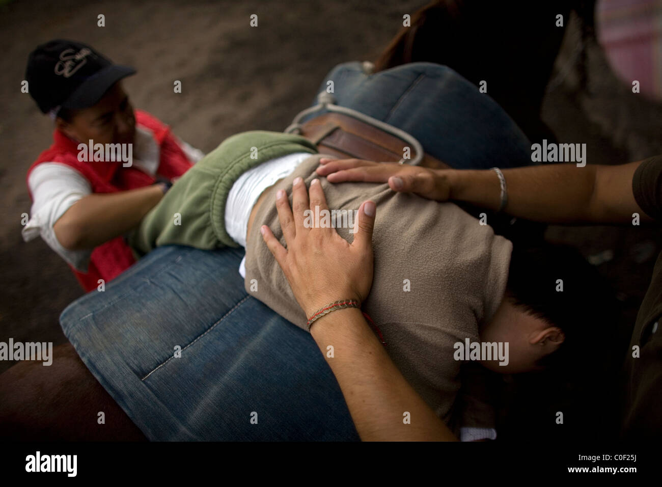Equine Therapeuten führen ein Junge, der infantilen zerebralen Lähmung durch Übungen leidet, wie er auf dem Rücken eines Pferdes Durin liegt Stockfoto