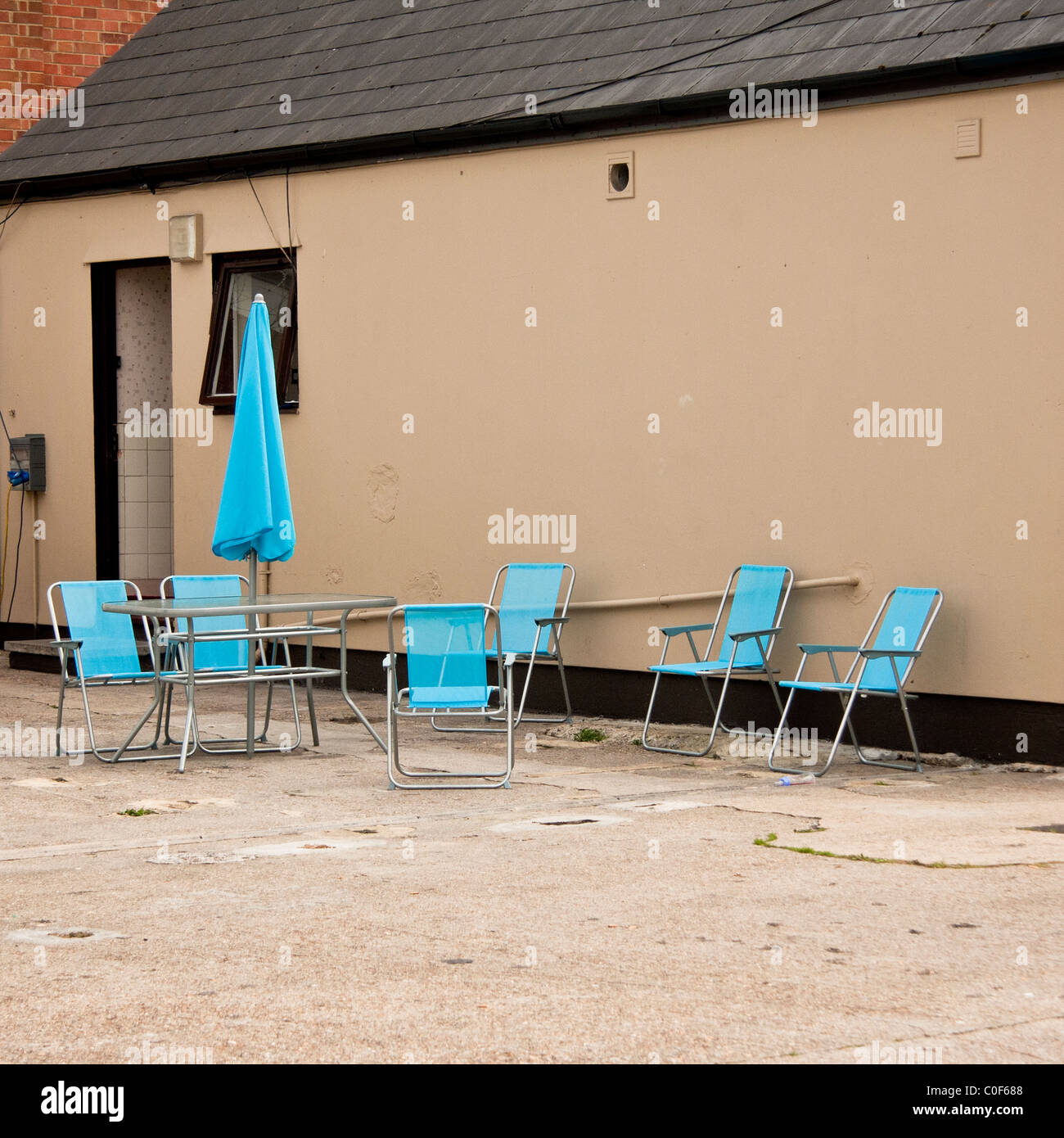 Blaue Stühle mit blauen Sonnenschirm im Garten eines braunen Hauses Stockfoto