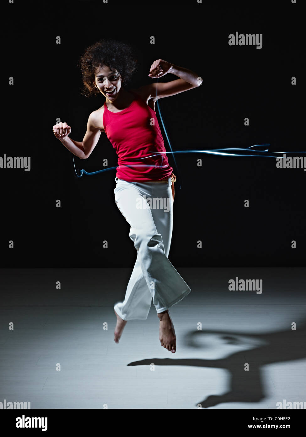 junge Erwachsene lateinamerikanische Frau springen und spielen mit led-leuchten Streifen auf schwarzem Hintergrund zu tun. Stockfoto