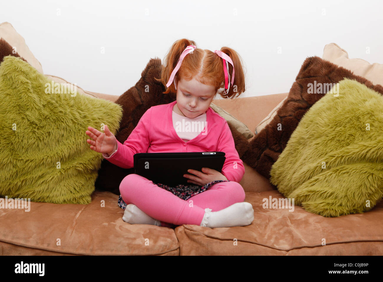 Kleines Mädchen auf einem Tablet Computer saß auf sofa Stockfoto