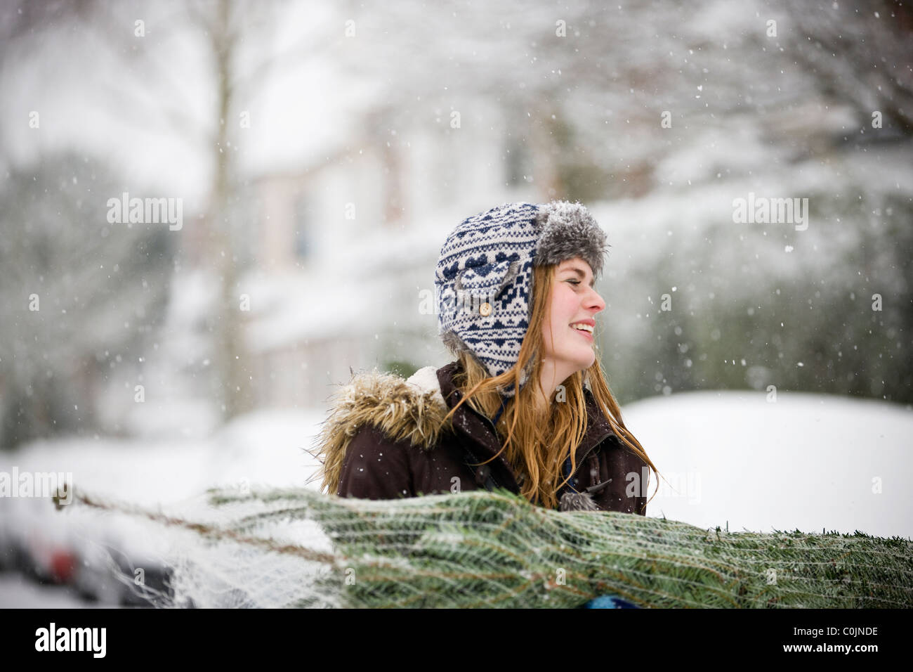 Eine junge Frau trägt einen Weihnachtsbaum im Schnee Stockfoto