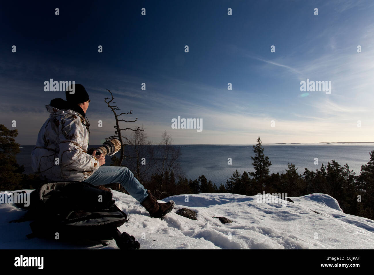 Mann sitzt auf dem Wasser im Winter von einem Berg mit einer Kamera in der Hand suchen. Stockfoto