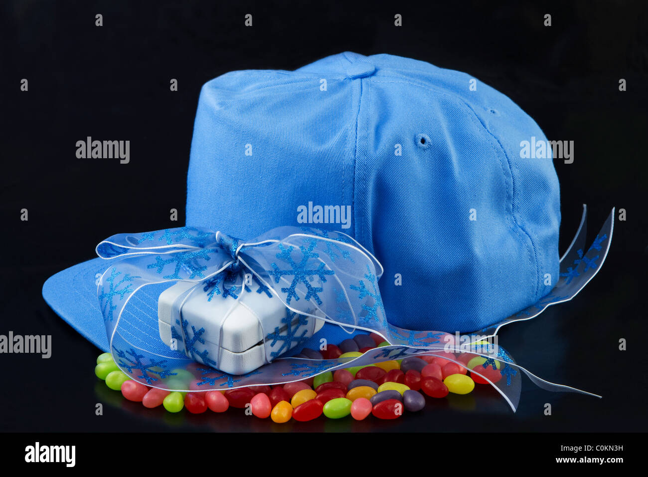 Blaue Baseball-Cap mit Geschenk wird auf Geleebohnen und vor einem schwarzen Hintergrund gelegt. Stockfoto