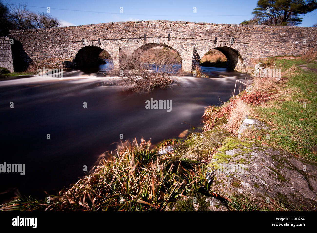 Langsame Exposition zeigt die Strömung des Flusses Dart unter der Brücke bei Post-Brücke, Dartmoor Stockfoto