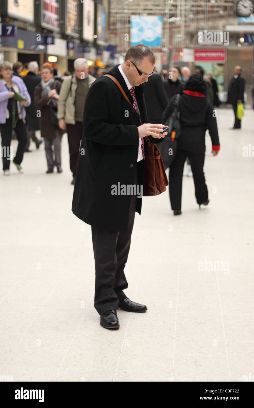 Geschäftsmann mit seinem mobilen PDA-Gerät am Bahnhof London Waterloo Stockfoto