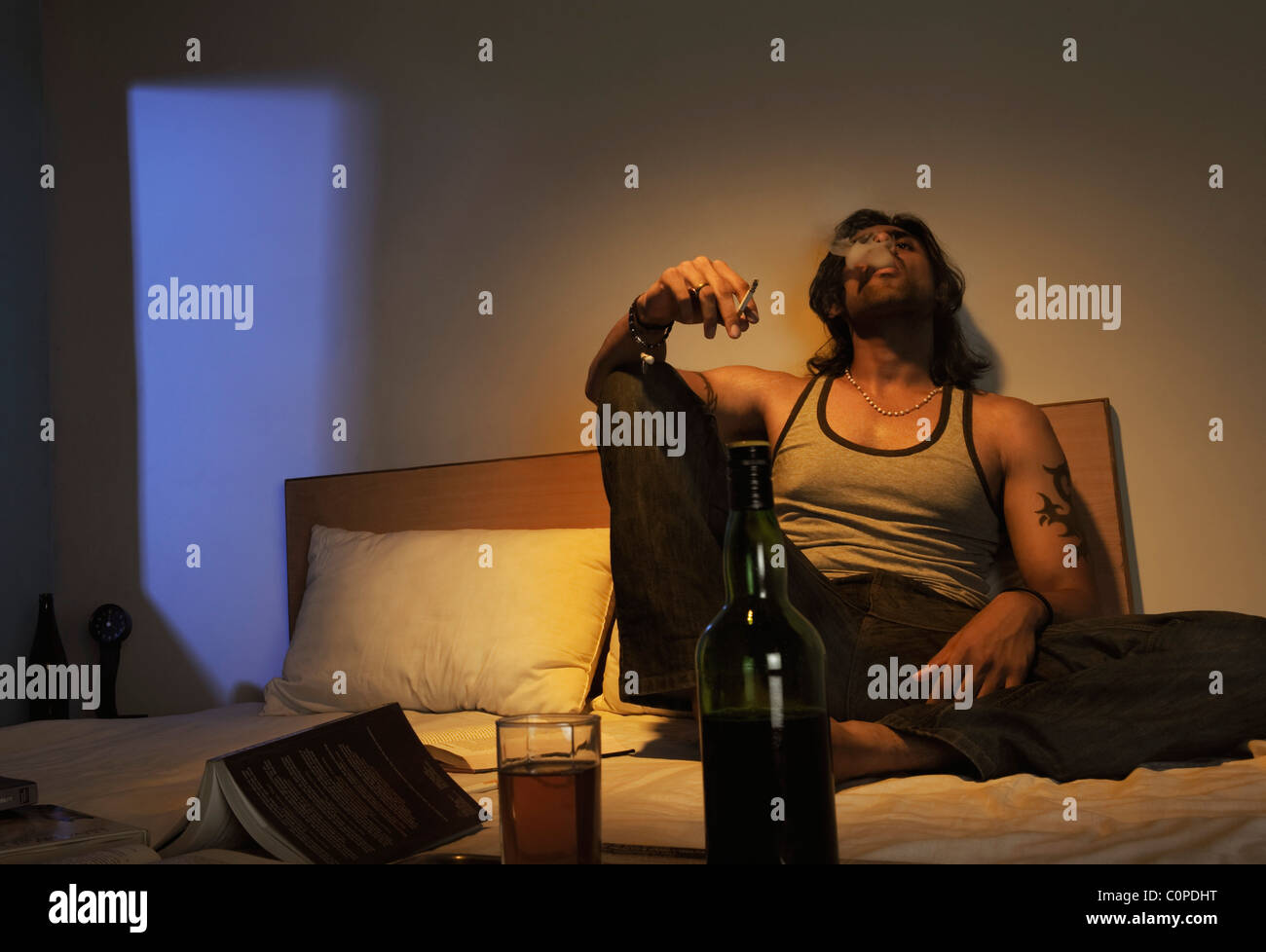 Mann auf dem Bett mit Wein Rauchen Stockfoto