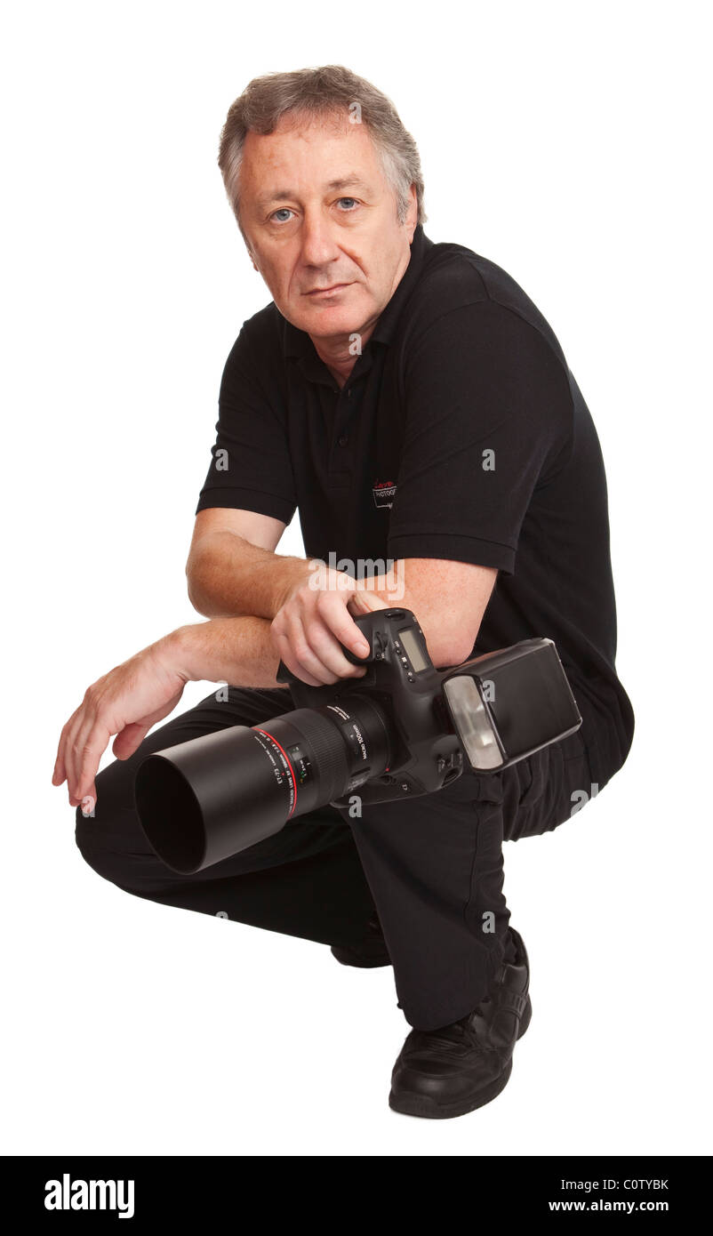 männlichen Erwachsenen gekleidet in schwarzen hockend hält eine professionelle DSLR-Kamera, vor einem weißen Hintergrund isoliert Stockfoto