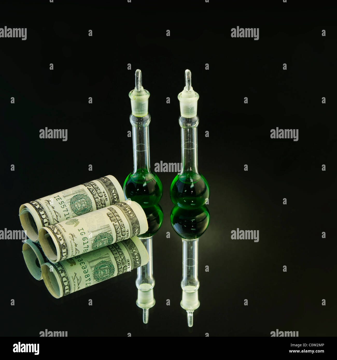Zwei Labor-Becher mit grüner Flüssigkeit stehen neben amerikanischen Währung auf einem Spiegel mit Licht flare auf grüne Becher. Stockfoto