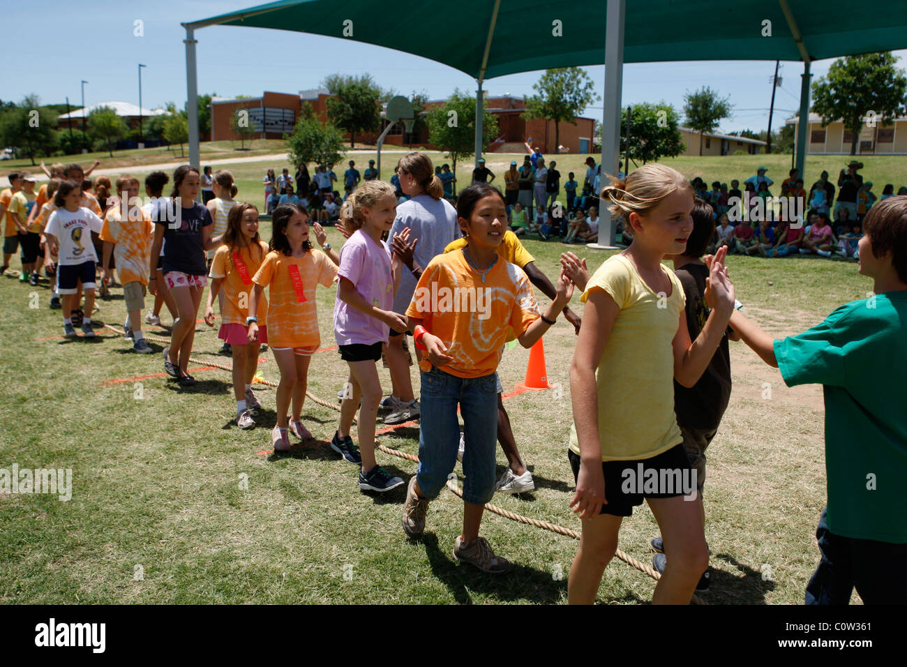 4. Klasse Mädchen und jungen zeigen Sportlichkeit durch schlagen der Hände mit dem gegnerischen Team nach Tauziehen Spiel in der Schule in Austin Stockfoto