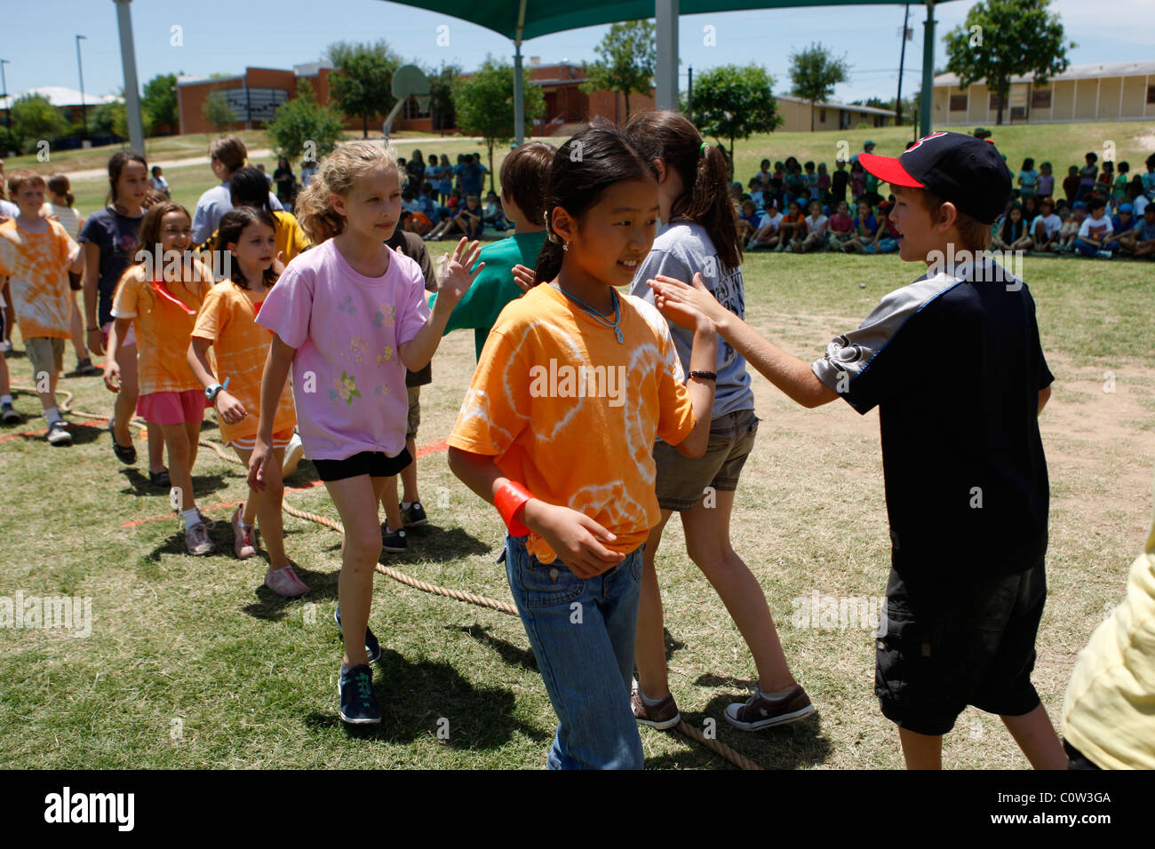 4. Klasse Mädchen und jungen zeigen Sportlichkeit durch schlagen der Hände mit dem gegnerischen Team nach Tauziehen Spiel in der Schule in Austin Stockfoto