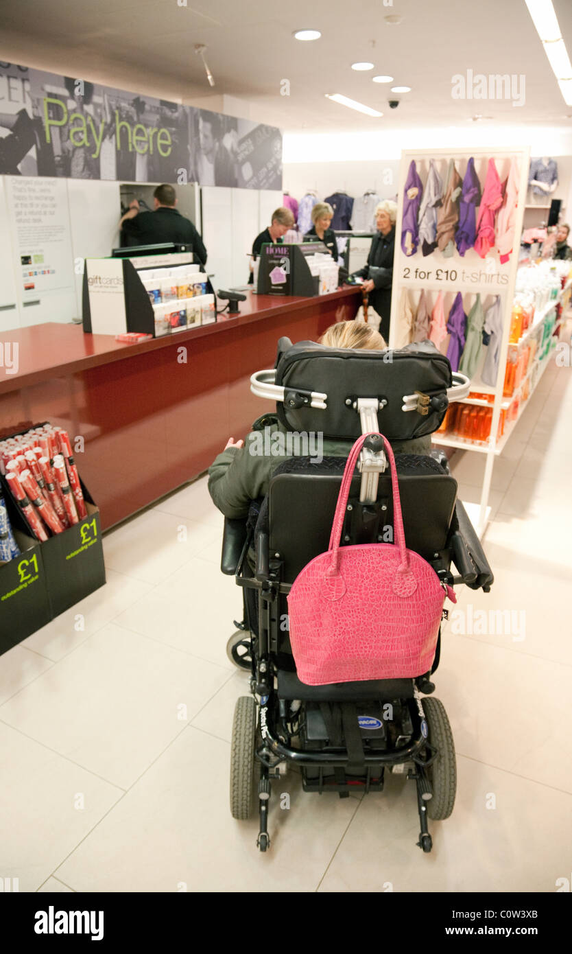 Behinderte junge Frau in einem Rollstuhl, die in einem Geschäft einkauft, Großbritannien; behindertengerechtes Geschäft UK. Stockfoto