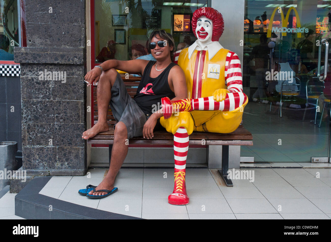 Eine balinesische Mann, sitzend mit dem Clown Ronald McDonald außerhalb der Sanur Beach-Filiale von McDonalds in Bali Indonesien Stockfoto