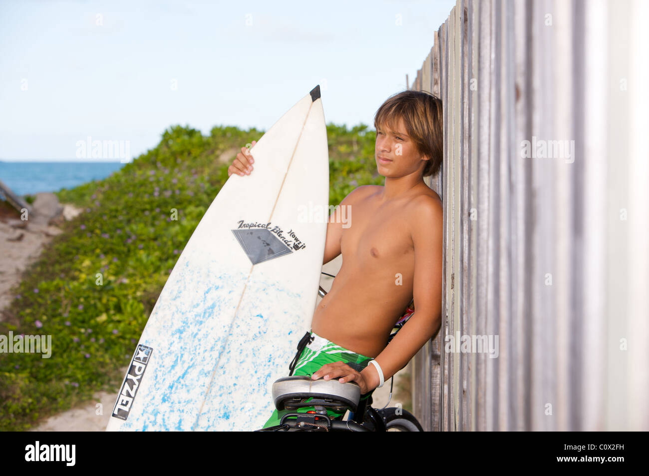 Ein Surfer junge ruht gegen einen Zaun Stockfoto