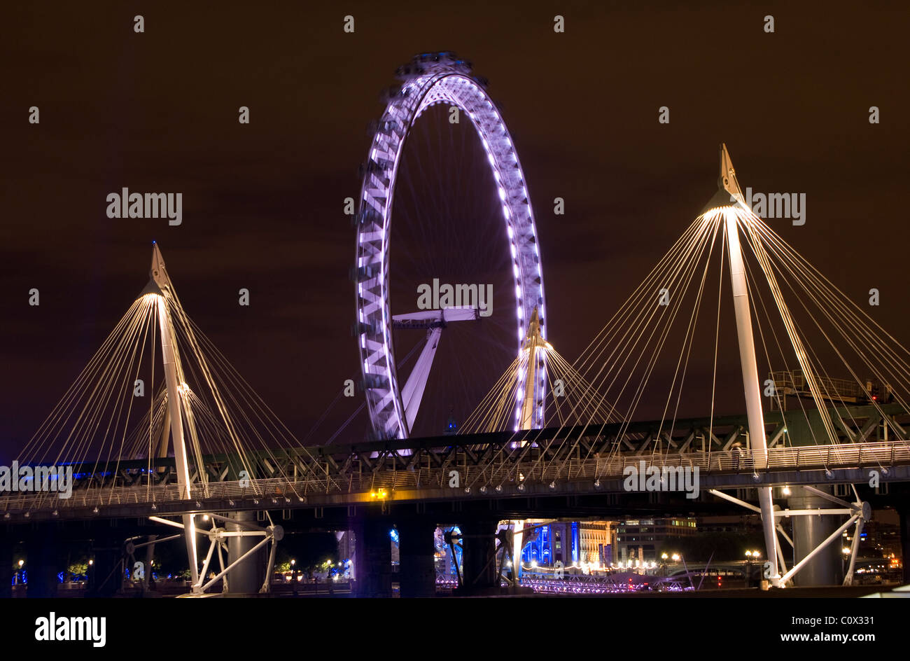 Dies ist die Millennium Bridge rund um eine sehr bunte London Eye bei Nacht. Stockfoto