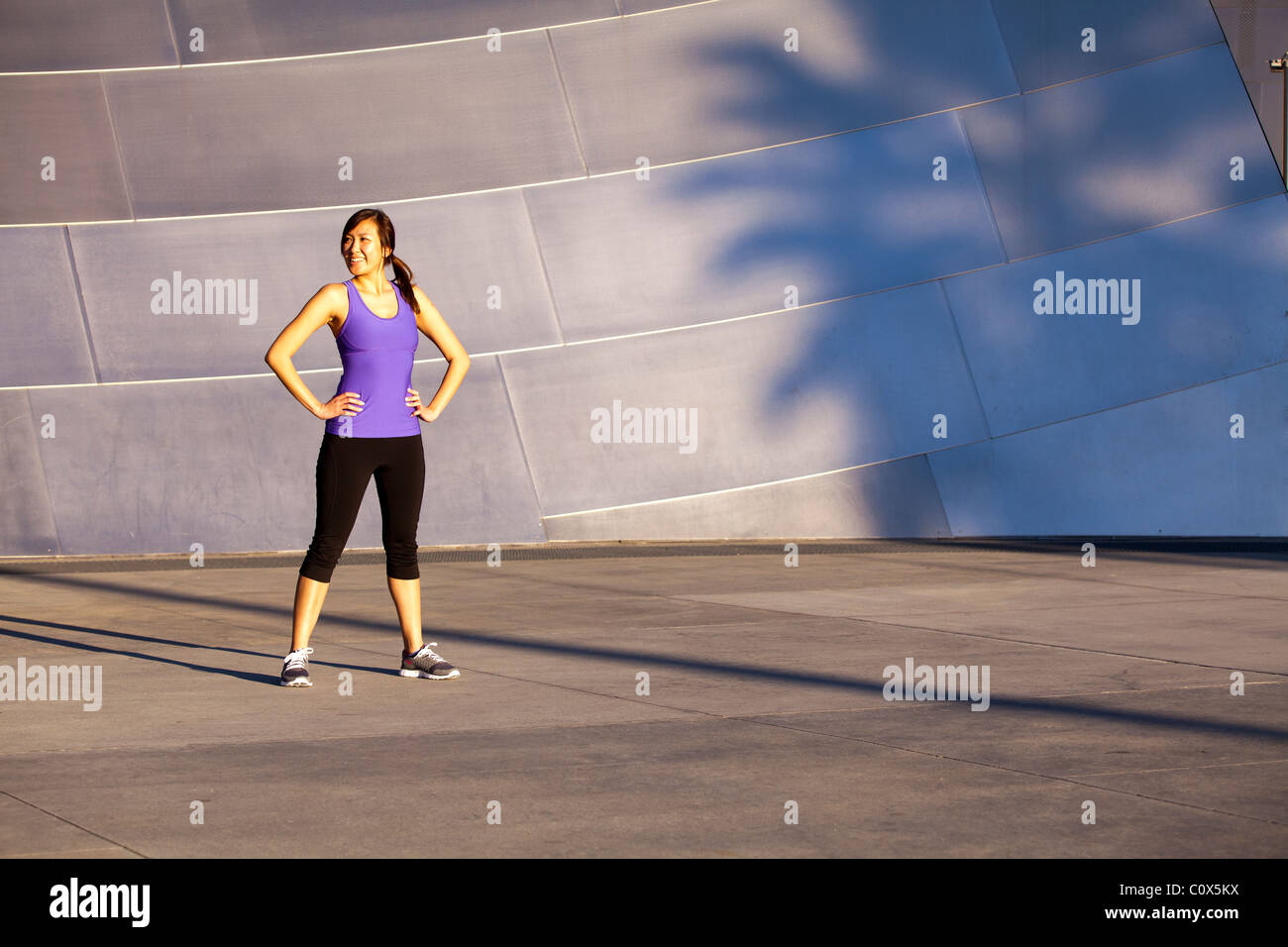 Asiatisch-amerikanische weibliche Läufer ruht vor Metall verkleideten Wand.  Lila Tank-Top und schwarze Hosen. Stockfoto