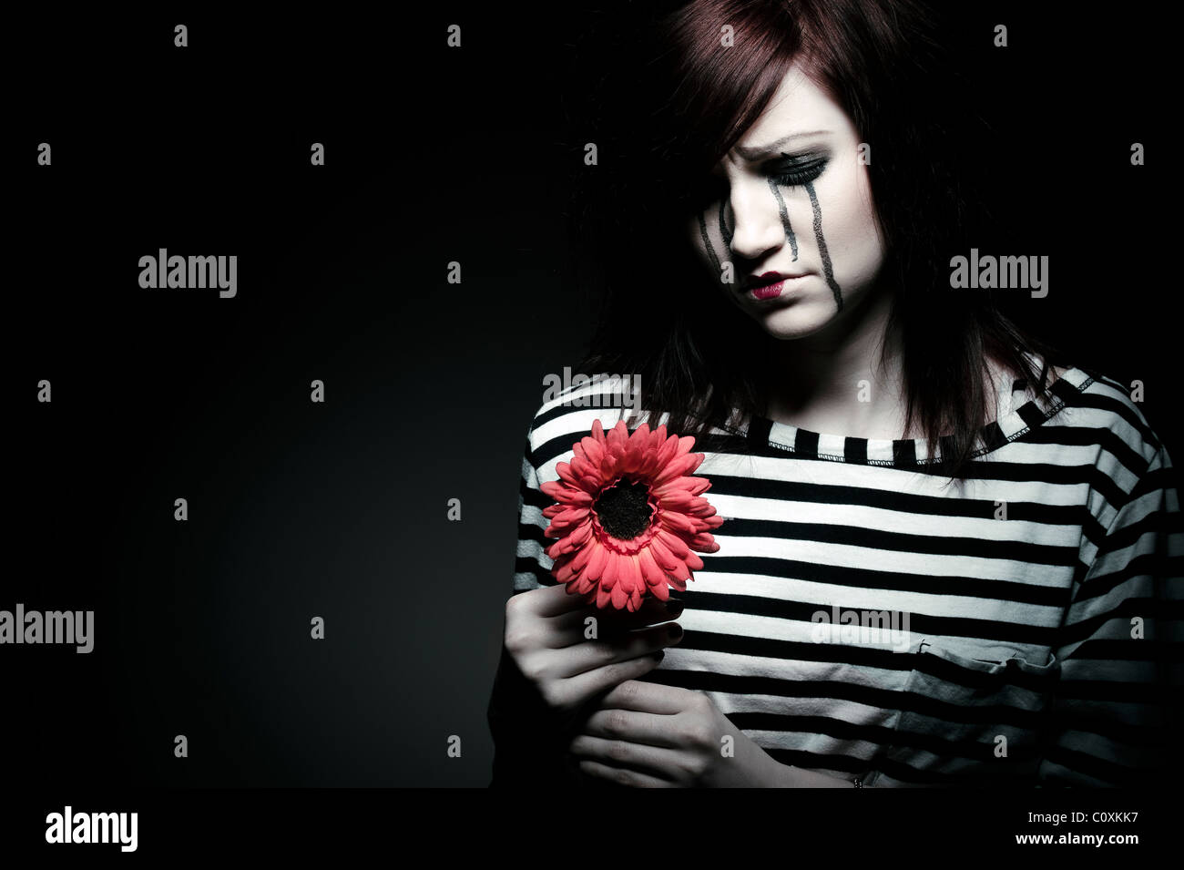 eine traurige weibliche MIME-Clown mit einer roten Blume Stockfoto