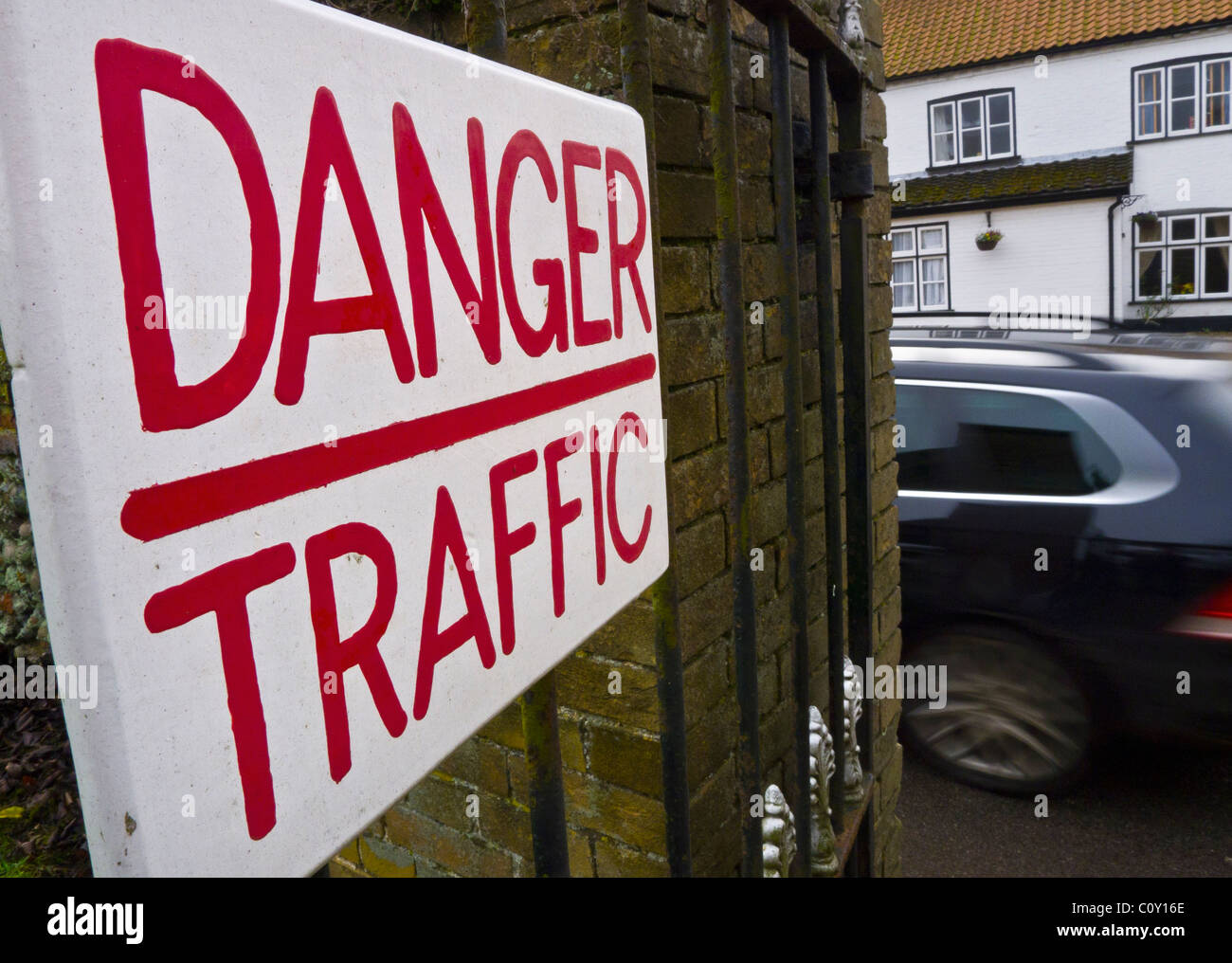 Eine Warnung Schild mit der Aufschrift "Gefahr TRAFFIC" mit einem fahrenden Auto auf der Straße hinter Stockfoto