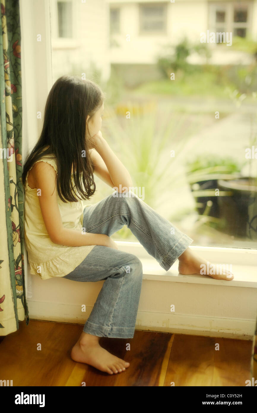 Mädchen sitzt durch Fenster an regnerischen Tag Stockfoto