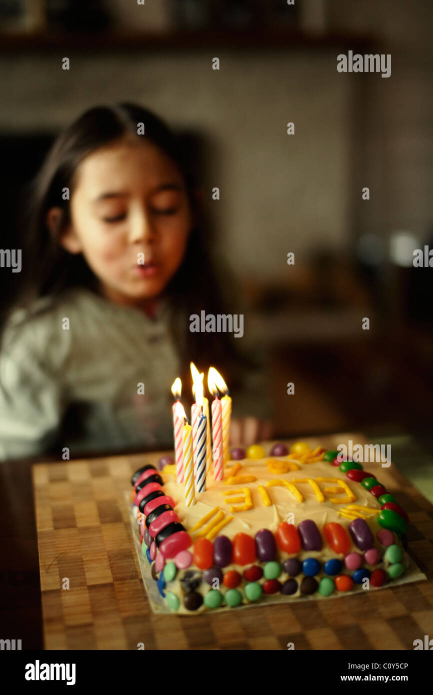 Mädchen bläst 7 Kerzen auf ihrem Geburtstagskuchen Stockfoto