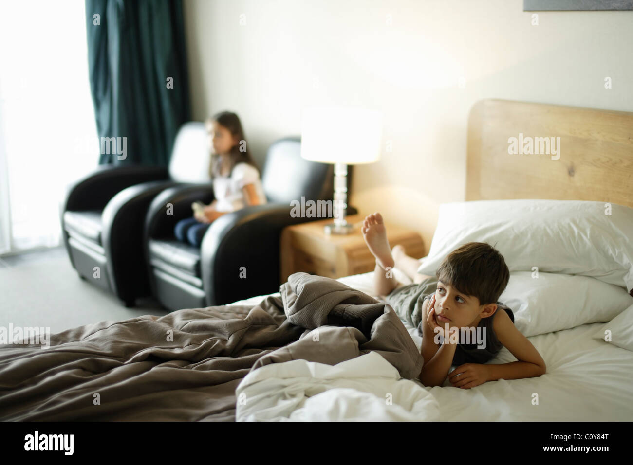Junge auf Bett und Mädchen auf Stuhl, gerade Wand montiert tv in einem Motelzimmer. Stockfoto