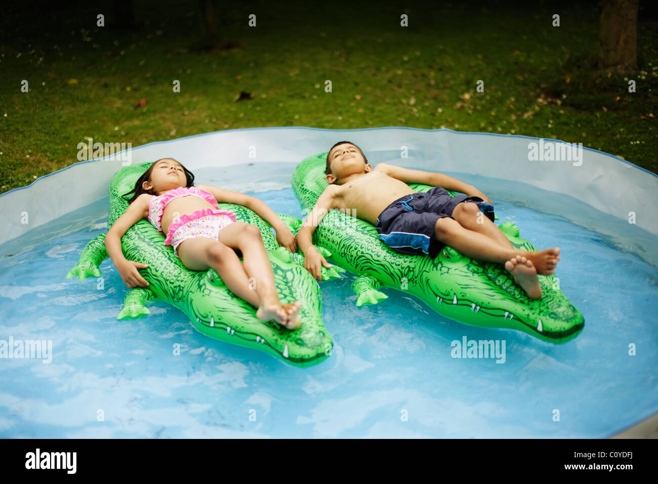 Jungen und Mädchen liegen auf aufblasbaren Krokodilen im Planschbecken schweben. Stockfoto