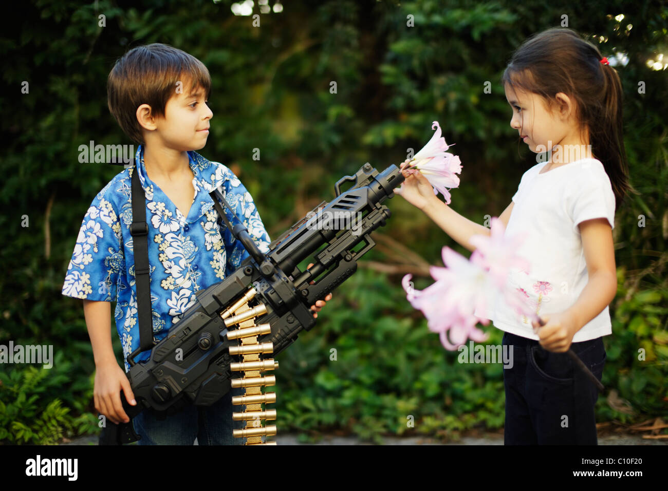 Fünf Jahre altes Mädchen legt Blumen im Lauf ihres Bruders Spielzeug Maschine Pistole Stockfoto