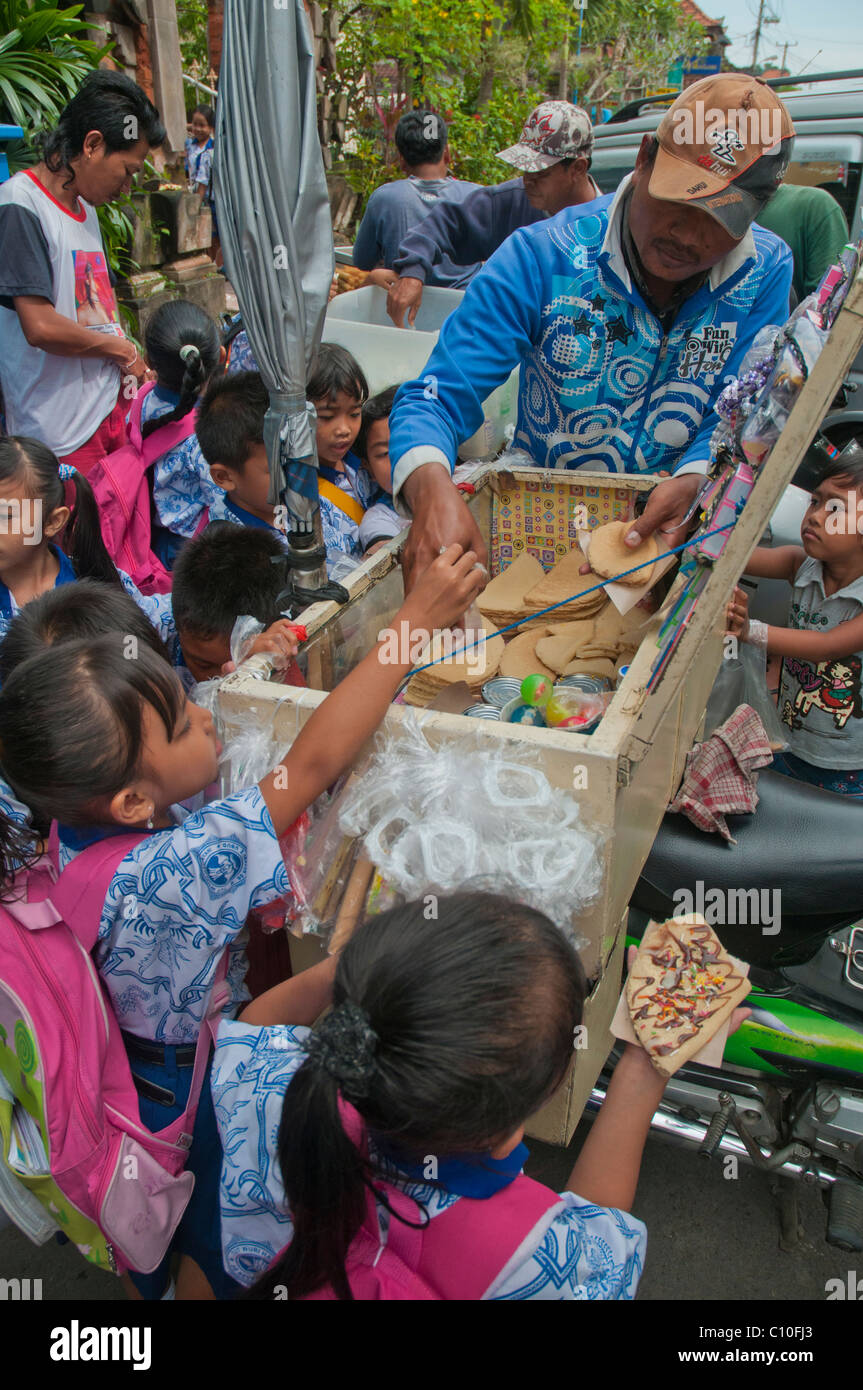 Indonesische Grundschulkinder kaufen, nachdem Schule behandelt von einem Straßenhändler außerhalb ihrer Schule in Ubud, Bali, Indonesien Stockfoto