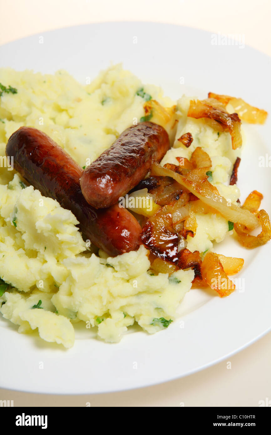 Traditionelle britische "Bangers and Mash" essen Würstchen mit Kartoffelbrei Petersilienkartoffeln und karamellisierten Zwiebeln auf einem Teller. Stockfoto