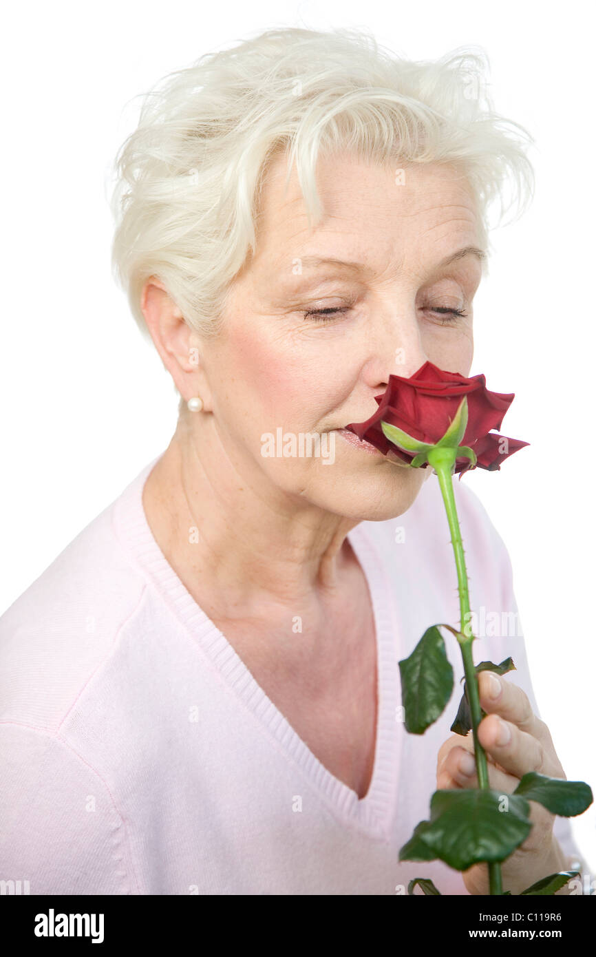 Eine reife Frau, die eine welke rote Rose riechen Stockfoto