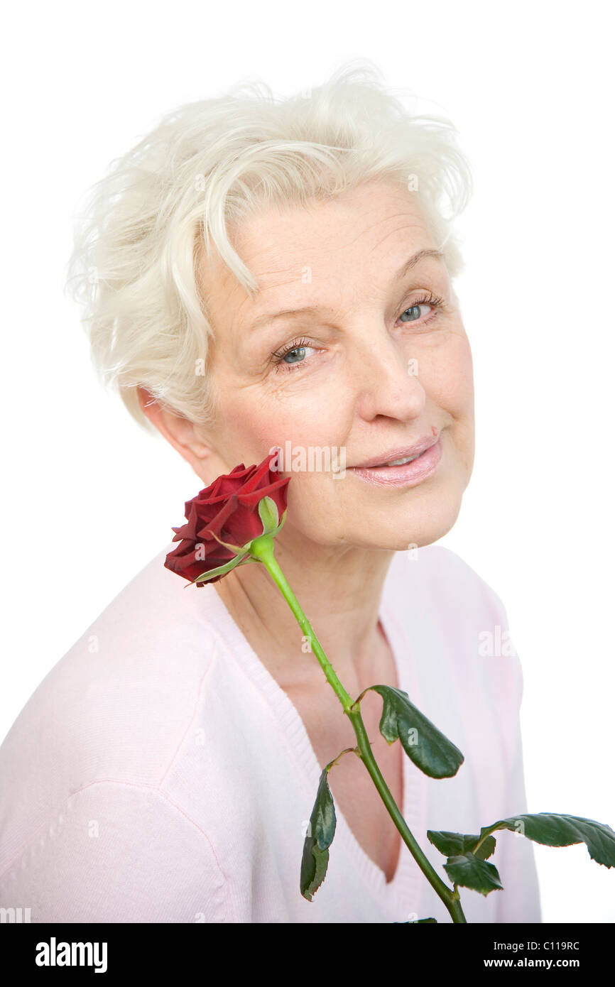 Eine reife Frau hält eine welke rote Rose auf ihr Gesicht Stockfoto