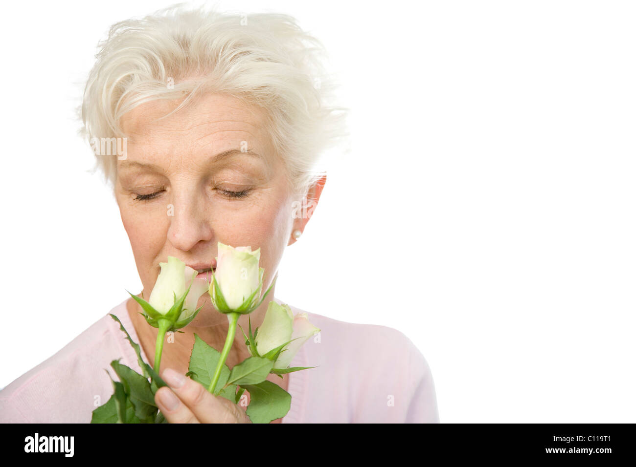 Eine reife Frau, die drei Rosa Rosen riechen Stockfoto