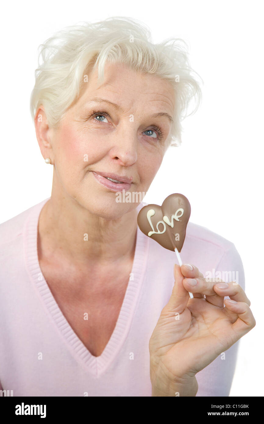 Eine reife Frau ein Schokoladenherz mit dem Wort "Liebe" in der Hand halten und schauen verträumt in die Ferne Stockfoto