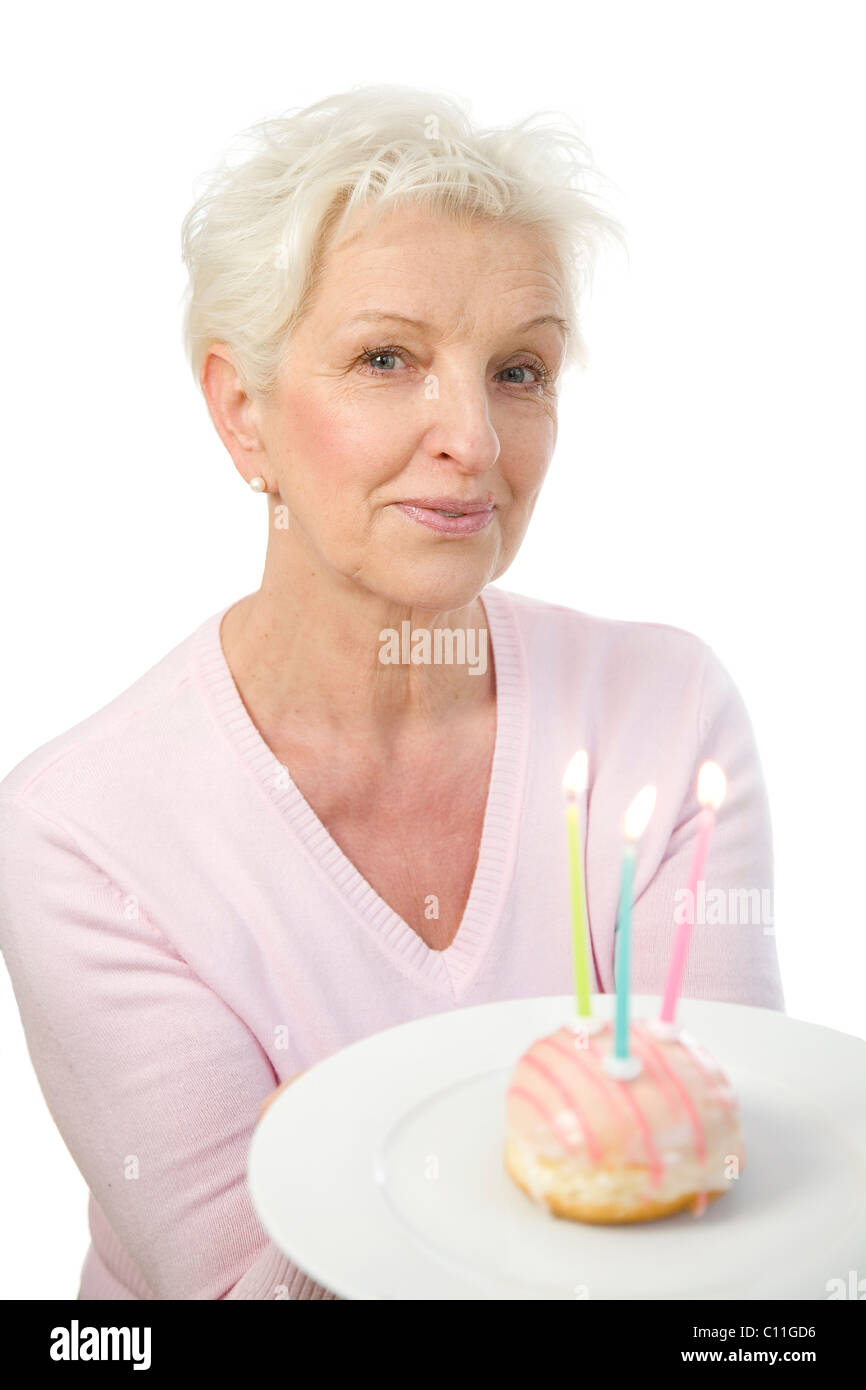 Eine reife Frau einen Teller mit einem Donut mit Kerzen in ihren Händen hält Stockfoto