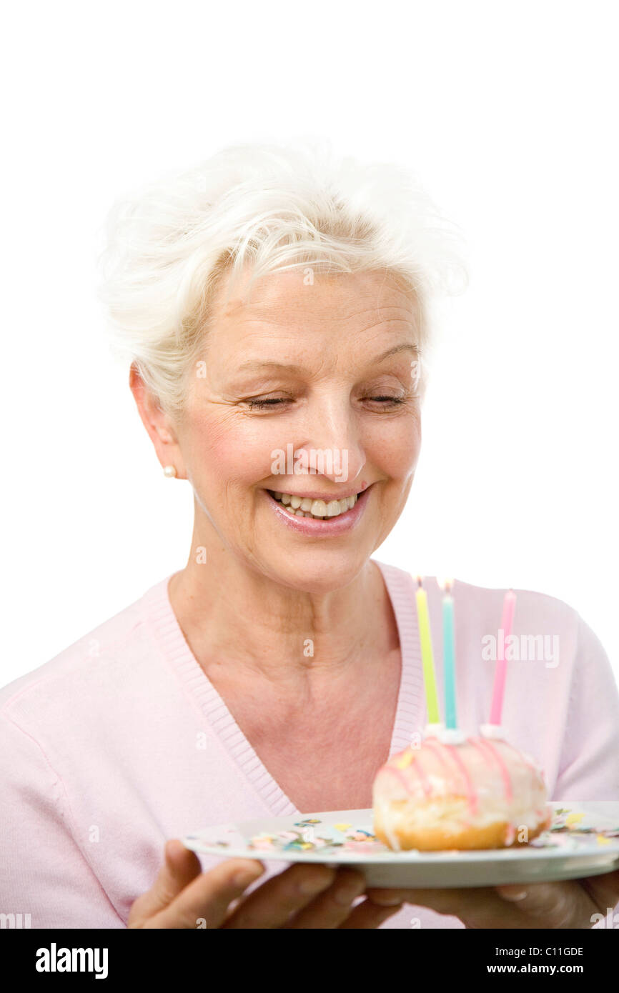 Eine fröhliche Frau einen Teller mit einem Donut mit Kerzen in ihren Händen hält Stockfoto