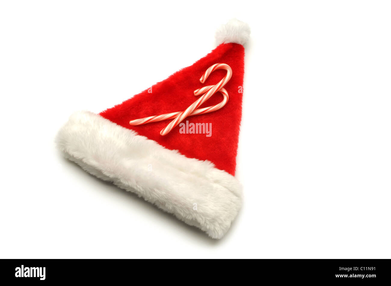 rote Weihnachtsmütze auf weißem Hintergrund mit Zuckerstangen Stockfoto