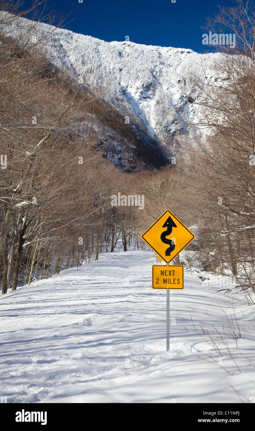 Foto einer Schnee bedeckten Straße führt auf einen Berg mit einem Schild im Vordergrund. Stockfoto